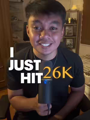 A young man with dark hair and a black t-shirt is holding a microphone and smiling at the camera. The text overlay "I JUST HIT 26K" is displayed in a bold white and yellow font.