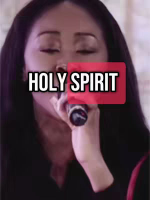 A woman with long dark hair is holding a microphone and singing. The text overlayed, 'HOLY SPIRIT' is in large, bold, white font, set against vibrant red rectangles, visually dividing the image and drawing attention to the text.