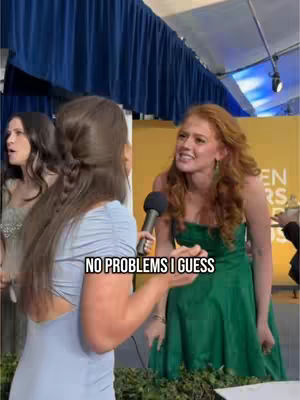 The cover image shows two women, one in the foreground with light blue clothing and her back mostly to the camera, holding a microphone as if interviewing. The other woman is facing the camera, wearing a green dress and a smile. They are standing in what appears to be a corridor with a golden background that reads "Golden Globes". A text overlay "NO PROBLEMS I GUESS" is placed on the image.