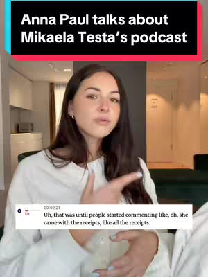 A woman is in the center of the image, gesturing with her right hand and talking. Text overlays at the top and bottom. The top text reads, "Anna Paul talks about Mikaela Testa's podcast" in a black box with a red bar. A second text box at the bottom contains white text on a black background and time stamp, the woman appears to be in an indoor apartment with a door and window behind her