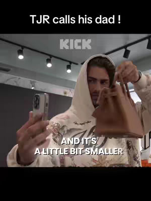 A man wearing a white hoodie holds a phone in one hand and a brown handbag in the other, looking toward the camera. The background includes a shop setting with overhead lights. Text overlays at the top and bottom.