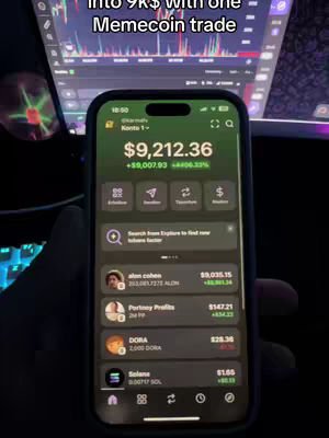 A person is holding a phone displaying a finance app with a green interface. The phone shows a balance of $9,212.36, with a large positive gain. The background is dark, featuring a computer screen displaying stock charts. Text stating 'Into 9k$ with one Memecoin trade' is overlaid at the top.