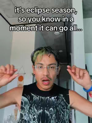 The cover image features a young man with short, dark hair with dyed green streaks and glasses. He wears a black tank top with a skull design. The background is a brightly lit room with a ceiling and a light fixture. Text overlayed on the top of the image reads, "it's eclipse season, so you know in a moment it can go all..."