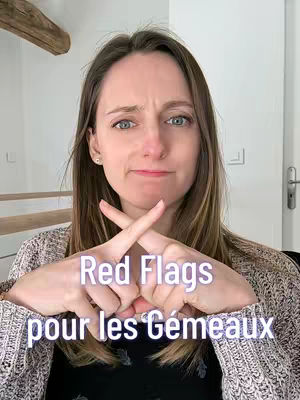 A woman with brown hair and blue eyes looks into the camera with a slightly furrowed brow. She crosses her index fingers in front of her chest. Overlayed text in a cursive font reads 'Red Flags pour les Gémeaux'. The background appears to be a soft white wall and a wooden beam.