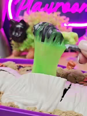 The cover image showcases a Zuru Horror House playset, with a green, claw-like hand emerging from under a white sheet, suggesting a mummy. The scene includes a purple tray filled with sand, rocks, and other elements of the playset in a dimly lit environment.