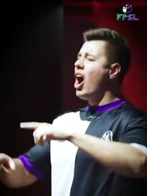 A man with short brown hair is captured mid-speech or action, mouth open with an intense expression. He's wearing a black and white two-tone shirt. The background is split, with a dark area on the left and a solid, deep red on the right side. A small logo of an 'FPSL' with a cat icon is located in the top right corner.