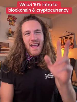 A man with long brown hair is giving a peace sign in a room, wearing a black t-shirt with text. Above him is red banner text. A cartoon is displayed on the left towards the back of him along with additional objects and wall decorations.