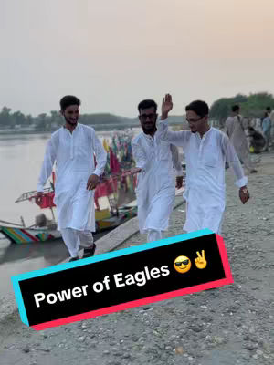 Three young men in white traditional clothing walk along a waterfront, with a river or lake and distant shoreline in the background. A colorful row of boats is visible beside them. A hook with black text and a sunglasses emoji overlayed.