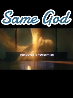 The image shows a scene with what appears to be a stage or installation. The text overlayed at the top states "Same God" in a curved fancy font with a white outline and blue fill , set against a black background. Below, there is an installation showing "YOU MOVED IN POWER THEN" in white text on a black rectangle with what appears to be a light source casting down and reflecting off the stage surface which is creating a reflection