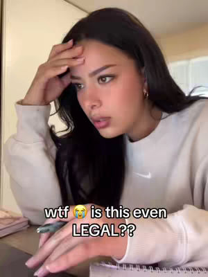 A young woman with long, dark hair and a light-colored sweatshirt is the central focus. Her expression suggests concern, as she has her hand to her forehead while looking at a laptop screen. Text overlayed on the image reads 'wtf π is this even LEGAL??' in bold, white font.