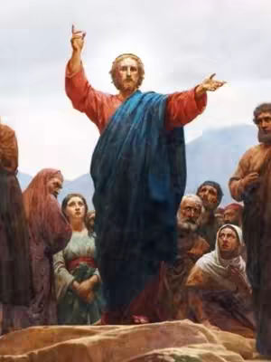 The image shows a classical painting of Jesus preaching to a crowd. Jesus, the central figure, is depicted with fair skin, long brown hair, and a beard, wearing a red robe and a blue cloak. He stands on a raised area, gesturing with his right hand raised towards the sky and his left hand open. The background is a slightly overcast sky. A crowd of people, men and women, are gathered around Jesus, watching intently. They are dressed in various robes and tunics. The overall composition is a traditional, religious artwork.