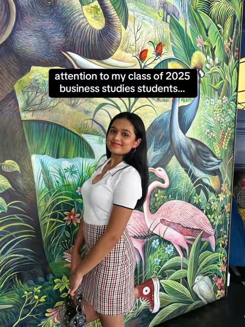 A person stands in front of a vibrant mural. The mural has a floral and animal theme. The person is wearing a white top and a plaid skirt. A text overlay is present at the top of the image.
