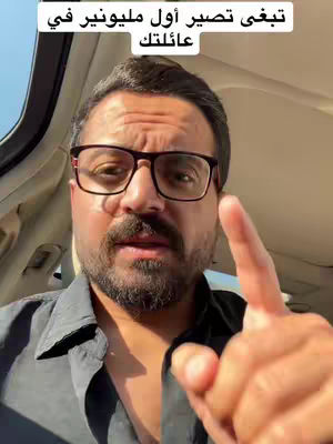 A man in a car points up with his index finger. Text in Arabic is overlaid on the image.