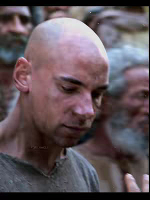 The cover image shows a man with a shaved head, seen from the chest up, looking downcast. He's surrounded by other men, some with beards, suggesting a crowd or setting. The lighting appears natural, maybe from a film scene, and the overall composition has a somber, possibly dramatic tone.