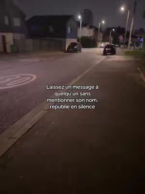 An outdoor shot at dusk shows a street with buildings on either side. In the foreground is the edge of a sidewalk and some asphalt. Cars are parked along the road, and streetlights illuminate the scene. Text is overlaid near the center of the image.
