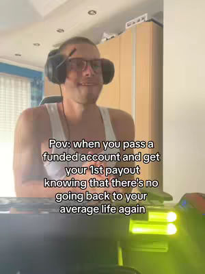 A man wearing glasses and headphones is smiling while looking at the camera, sitting in a chair with a desk and computer setup in front of him. Text overlayed on the image, describing the moment of getting a payout from a funded account.