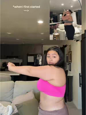 A woman in a pink sports bra poses with her arms extended in front of a living room setting with cream-colored couches and a separate inset image of the same woman in athletic wear from presumably an earlier stage in her fitness journey. Overlay text points to the inset image.